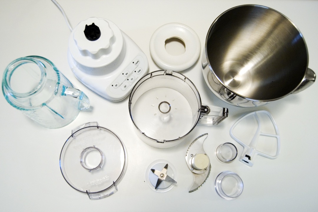 A blender base laid out with its blender jar, food processor bowl, S-blade, slicing disc and mixer bowl