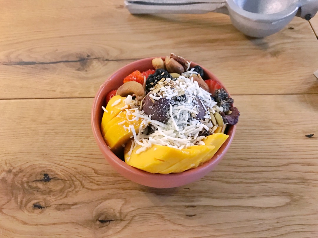 An acai bowl with a dark purple base topped with mango, berries, cashews and shredded coconut on a wooden table