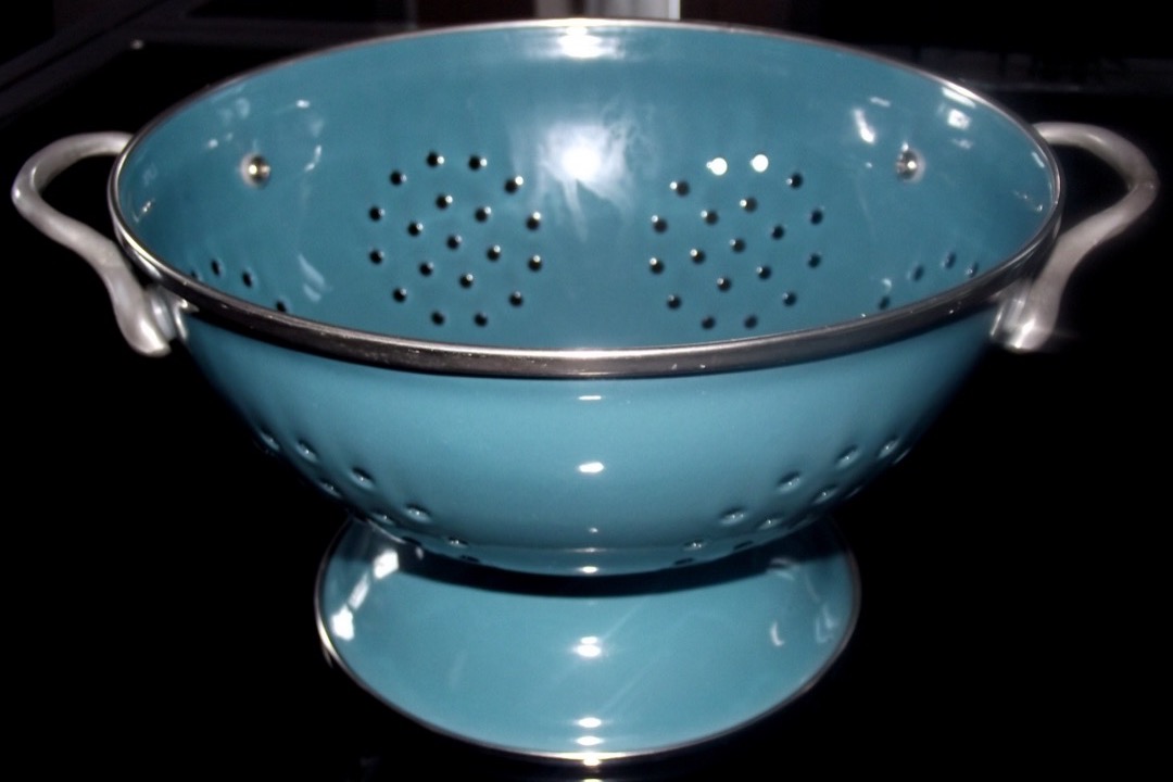 A footed enamel-and-steel colander on a counter, showing its perforation pattern and pedestal base