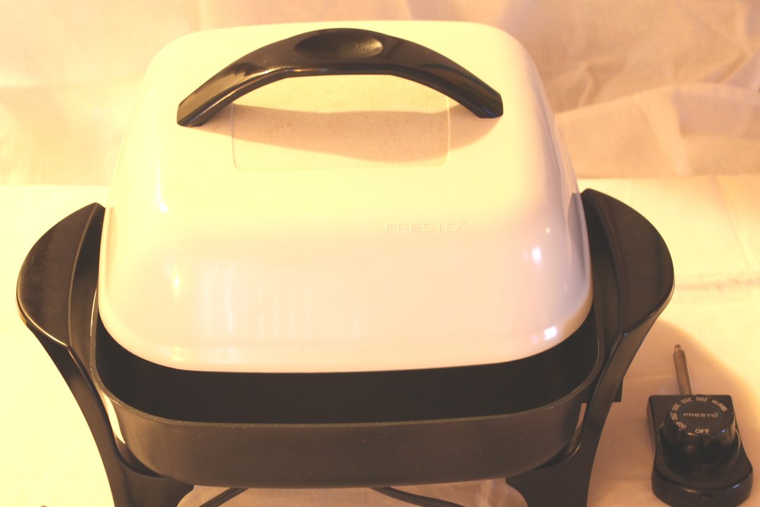 A square electric skillet with a white domed lid and a removable heat-control probe