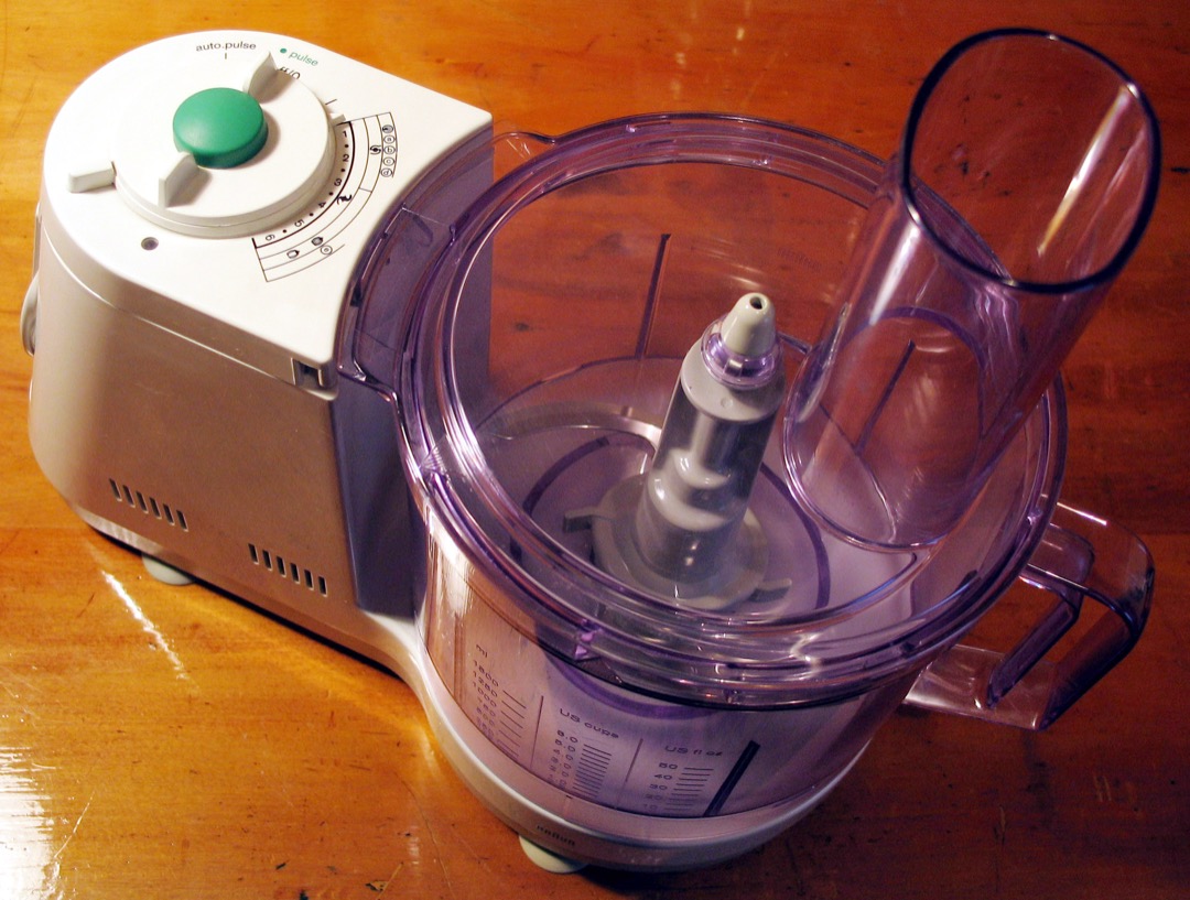 A food processor on a kitchen counter with its work bowl, S-blade and feed tube assembled