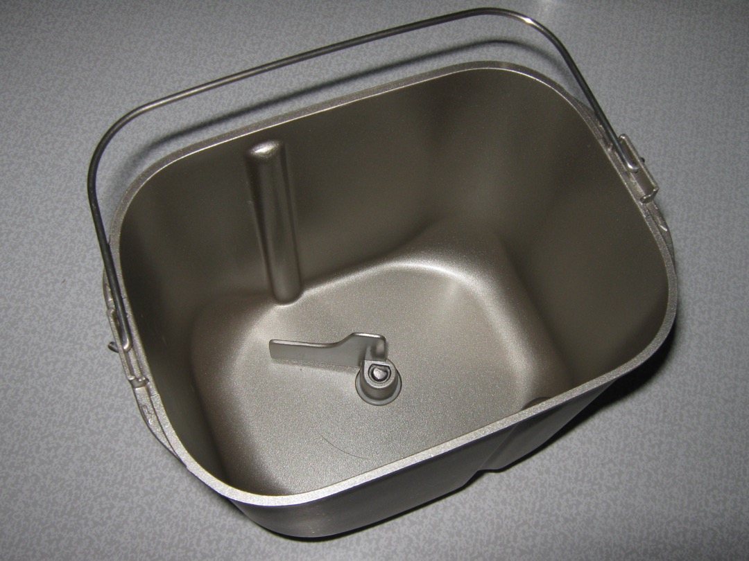 A bread machine's removable baking pan with its kneading paddle, seen from above