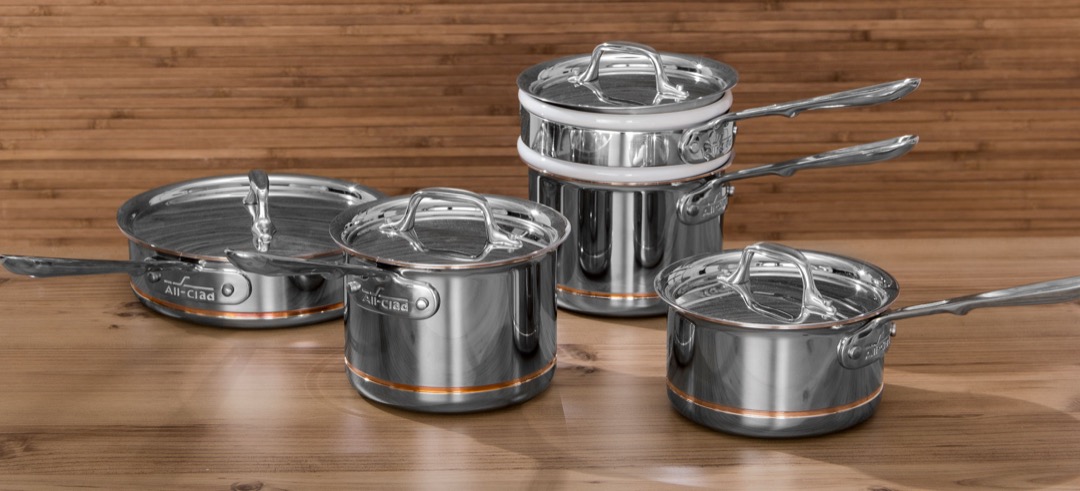A stainless steel cookware set of saucepans and a saute pan with lids on a wooden counter