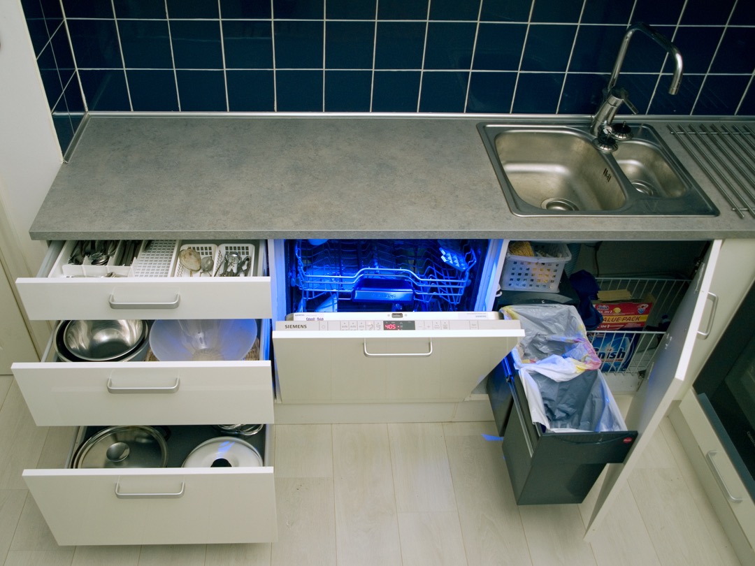 An integrated dishwasher pulled open between white kitchen drawers, its cabinet-matching door panel folded down to show the controls along the top edge