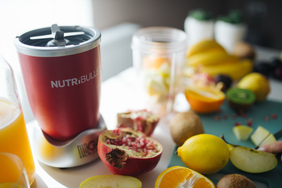 A red countertop personal blender on a bright kitchen counter surrounded by cut fruit