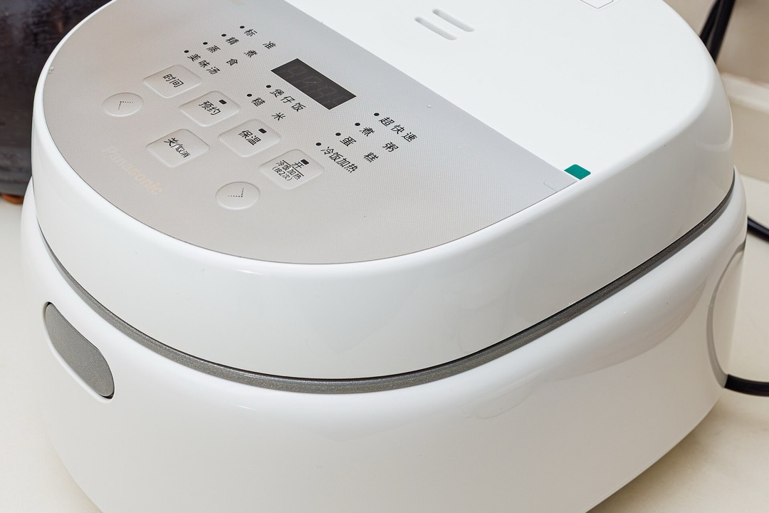 A white digital rice cooker with a control panel and lid latch sitting on a kitchen counter