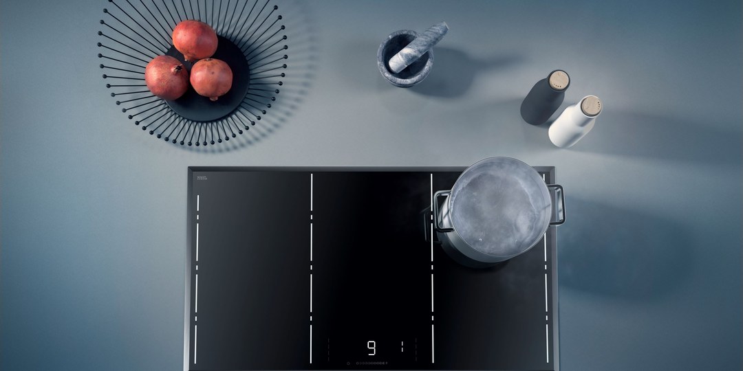 A heavy lidded pan sitting on a black glass-ceramic cooktop, photographed from directly above