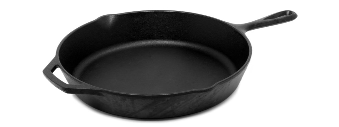 A black cast iron skillet with a loop handle and a helper handle, photographed on a plain white background