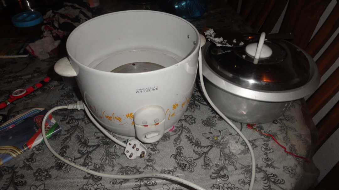 An electric rice cooker with its lid open and inner pot removed, showing the heating plate and the interior of the cooker body