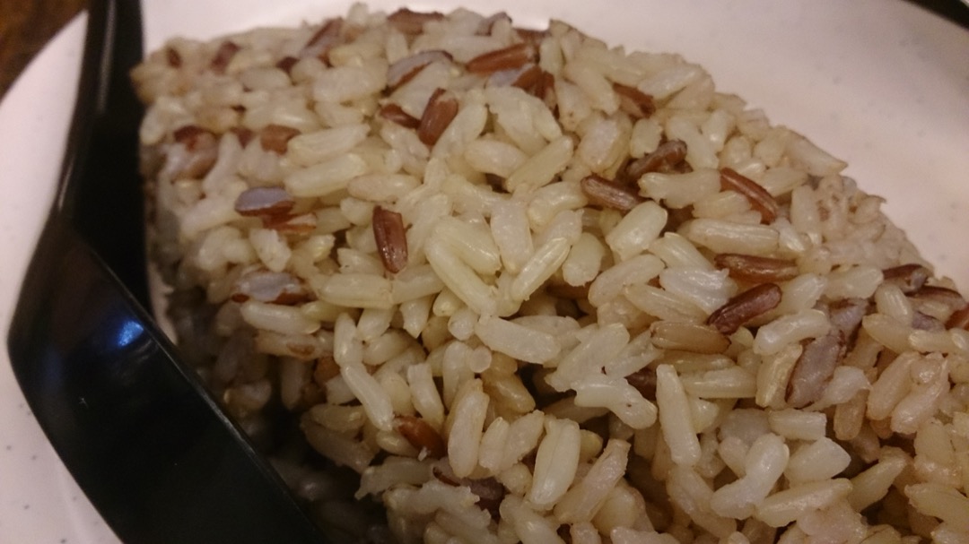 Cooked whole-grain brown rice with visible tan bran, served on a plate