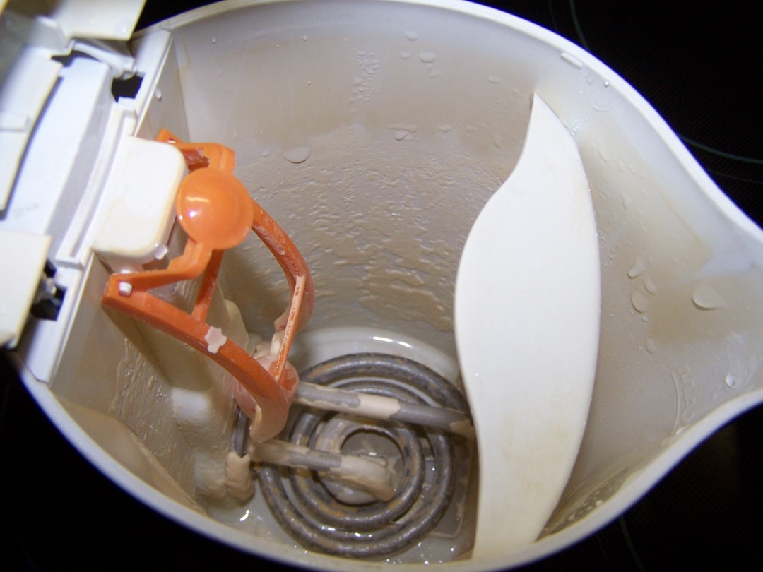 The inside of an electric kettle with the lid open, showing an exposed coiled heating element covered in pale mineral scale
