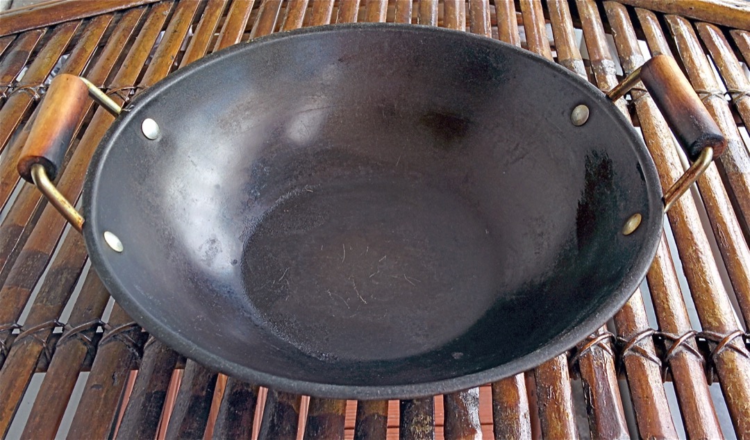 A dark, well-seasoned two-handled carbon steel wok photographed from above showing its patina