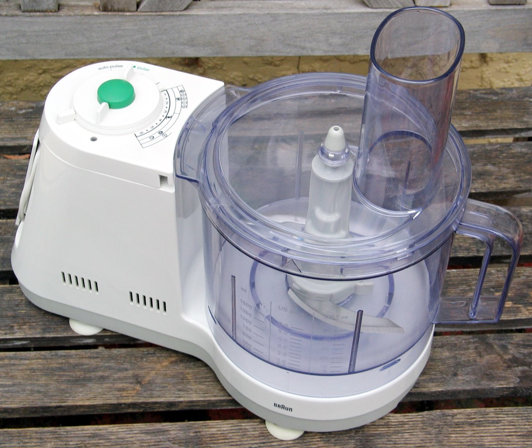 A white Braun food processor on a wooden surface with the S-blade seated in the clear bowl, the feed chute at the back and capacity markings up the side of the bowl