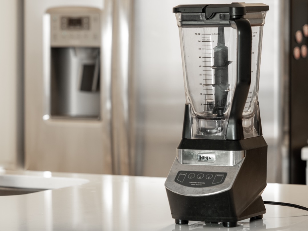 A Ninja blender on a kitchen counter with the stacked blade assembly standing inside the clear pitcher