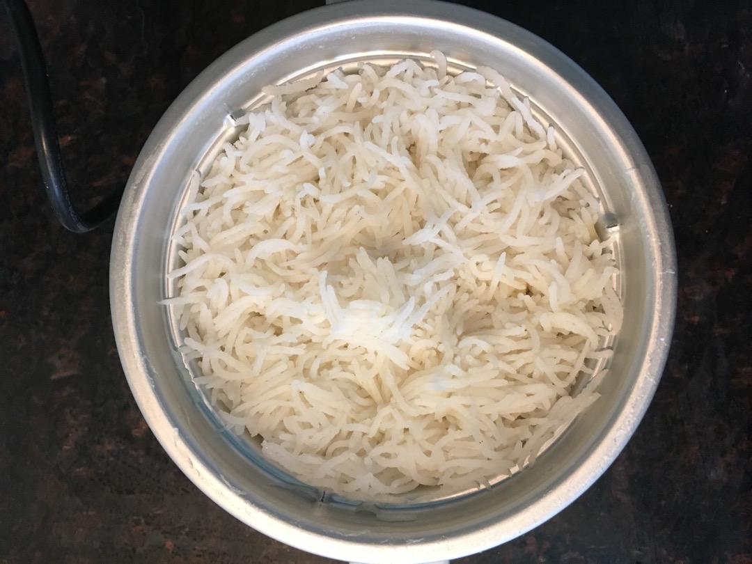 Freshly cooked long-grain white rice in the metal inner pot of an electric rice cooker, seen from above