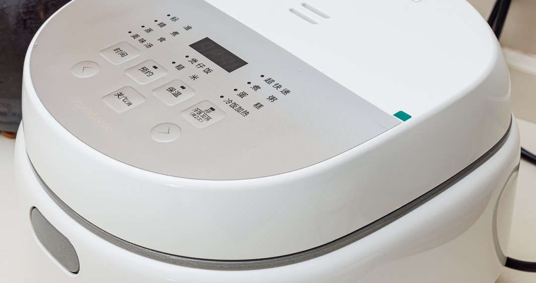 The control panel and hinged lid of a white digital rice cooker, photographed at an angle on a kitchen counter