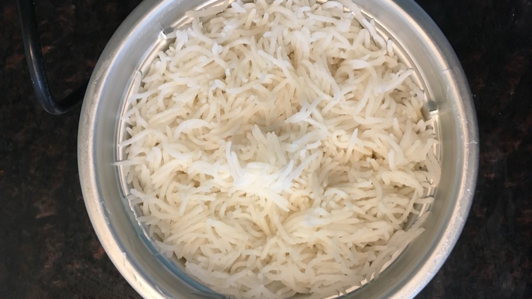 Overhead view into the stainless steel inner pot of an electric rice cooker filled with finished long-grain white rice