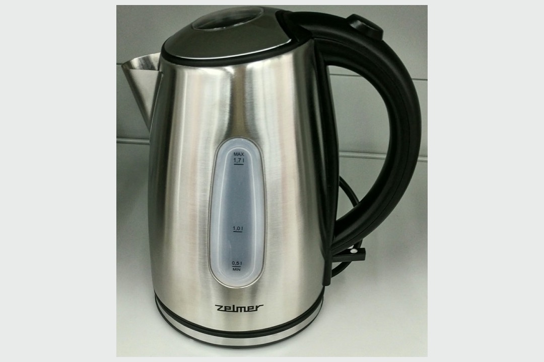 A brushed stainless steel electric kettle with a black handle and a translucent water-level window on a light countertop