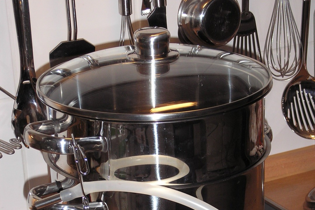 A stainless steel three-tier steam juicer with a tempered glass lid and drain hose sitting on an induction hob