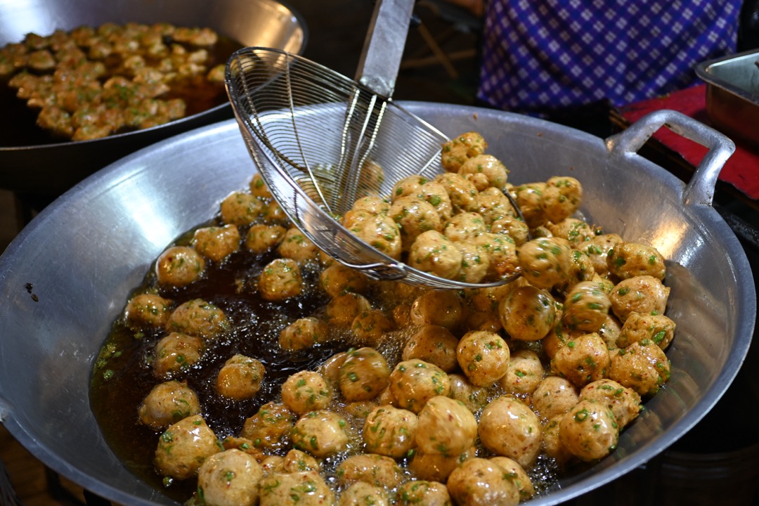 Golden fried fritters in a wide two-handled wok of hot oil, with a wire skimmer lifting a batch out