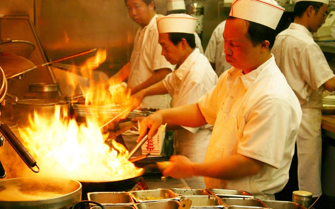 Chefs on a restaurant wok line, with flames leaping out of a wok over the burner